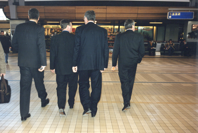360059 Afbeelding van een viertal mannen in donkergrijze pakken in de Stationshal te Utrecht.